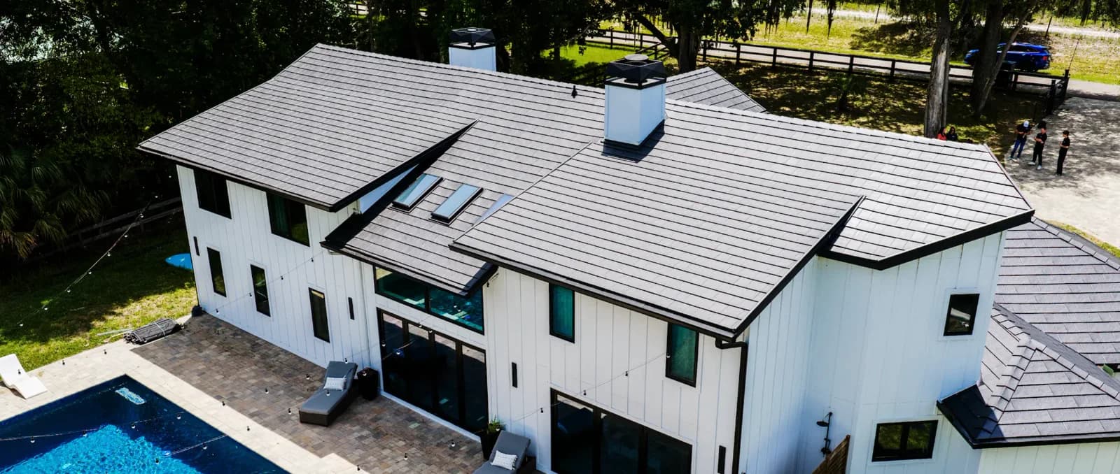 Aerial view of a modern white home with a dark Metlok metal roof and pool