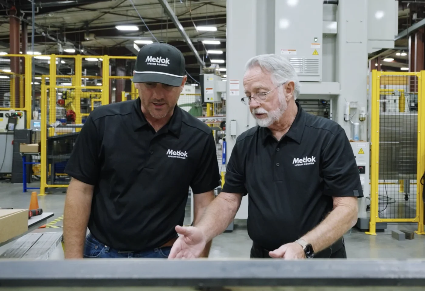 Two Metlok team members reviewing a metal roof panel on the factory floor.